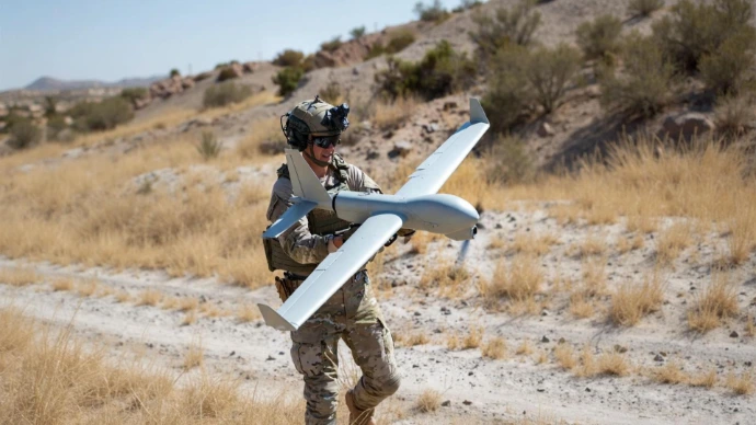 Ein Mann hält eine taktische Aufklärungsdrohne in einer wüstenartigen Umgebung.